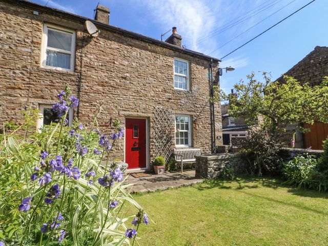 A stone house with a red door a garden bench a stone wall and flowering plants at Tiplady Cottage Bainbridge near Hawes