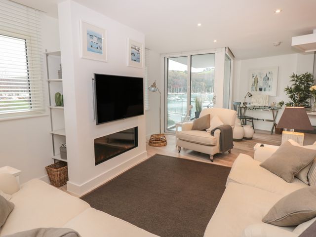 A living room with sofas a wall-mounted TV fireplace and a view of boats through glass doors at 2 Sails in Dartmouth