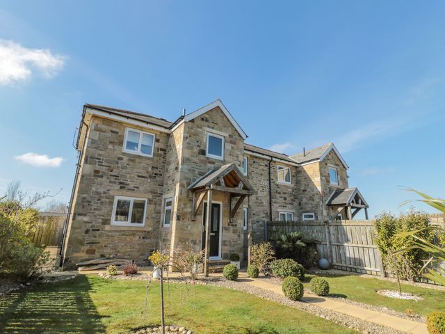 A stone house with a garden and wooden fence under a clear sky at Cushat House Stamford near Embleton