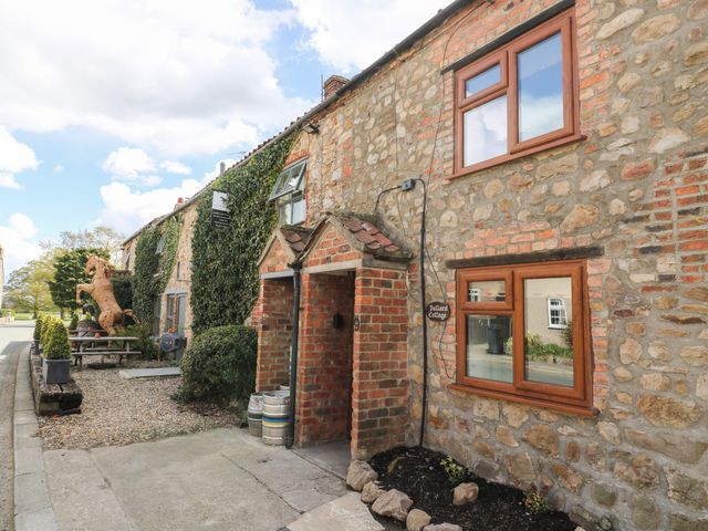 A stone cottage exterior with wooden framed windows and a small covered entrance at Pollard Cottage in Kirkby Fleetham near Northallerton