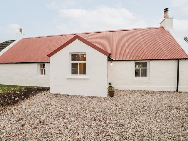 A view of a white cottage with a red corrugated roof and gravel yard at Lily Collies in Bogmoor near Fochabers