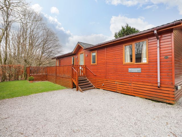 A wooden lodge with a small porch and steps on a gravel area next to green grass and trees at Wainwright Lodge Kirkstone 27 Limefitt Park near Windermere