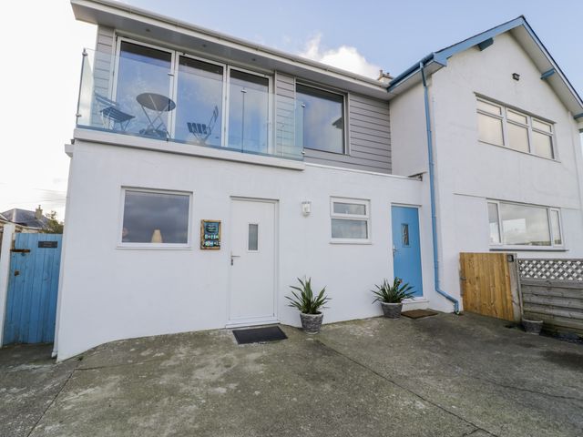The exterior of a two story house with two entrance doors and a balcony with chairs and a table at Porth Penwaig in Nefyn