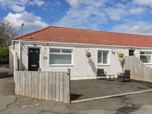 A single story house with a red tiled roof two black chairs and a small table outside and hanging flower baskets at Shore View in Kinghorn