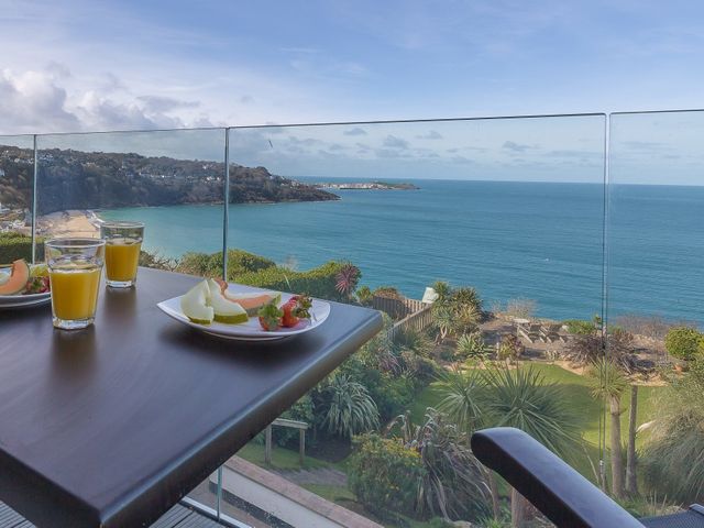 A balcony table with plates of fruit and glasses of juice overlooking the ocean and a garden at Pelagos in Carbis Bay