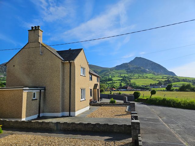 A gravel and paved driveway beside a two story house with a mountain and green fields in the background at Mor a Mynydd in Trefor