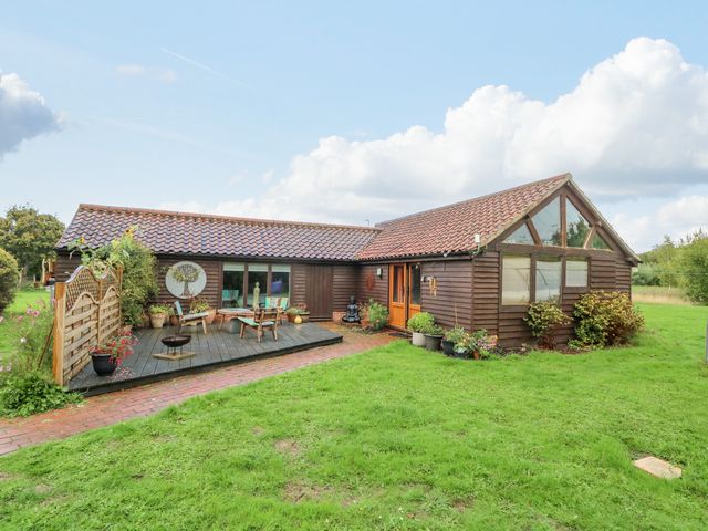 A single-story wooden house with a tiled roof a wooden deck with outdoor furniture and plants on a lawn at The Lodge in Hickling near Catfield
