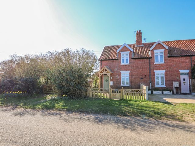 An exterior view of a brick house with white framed windows a wooden front gate and bushes at Meadow View in Sedgeford