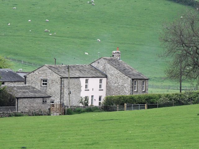 A stone cottage with a tiled roof in a grassy field with sheep grazing in the background at 3 Hull House Cottage in Hellifield