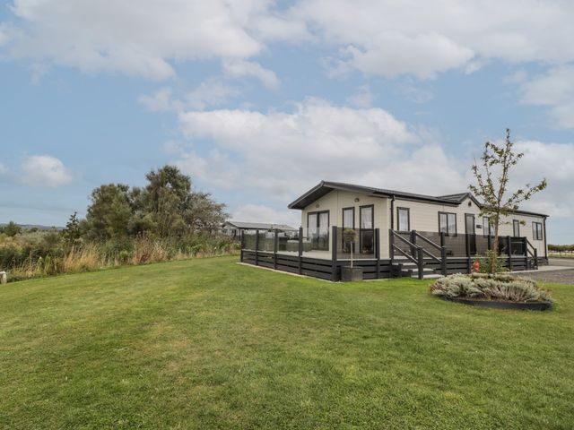 A modular or manufactured home with a fenced deck on a manicured lawn with trees and shrubs at 14 Fairways in Burnham-On-Sea