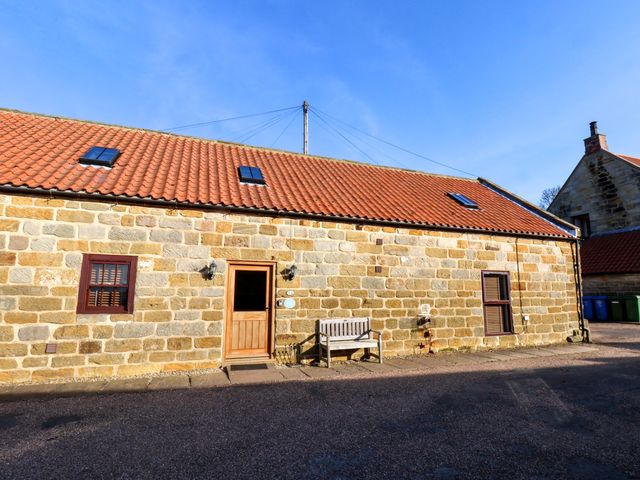 A stone building with a red tiled roof windows a wooden door and a bench outside at The Old Dairy Ellerby in Runswick Bay