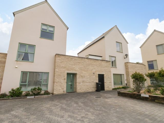 Three modern two story houses with green window frames and stone wall facades with a paved driveway and some plants at Pebbles Reach in Fortuneswell