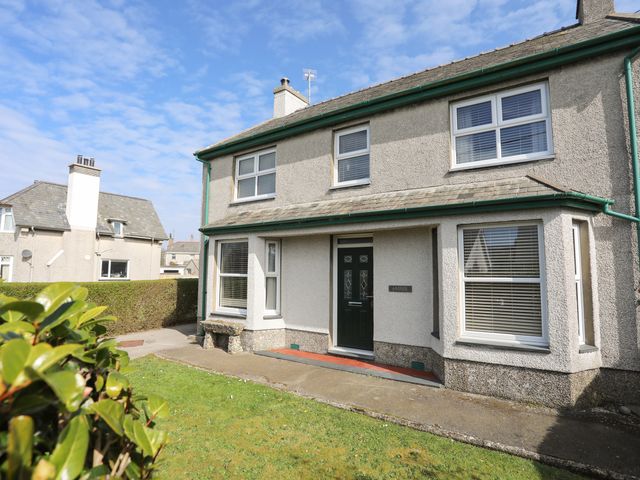 A grey two-story house with a black front door and multiple windows surrounded by a hedge and lawn at Arddol in Morfa Nefyn