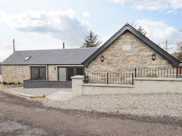 A single-story stone house with a gabled roof and gravel driveway at The Steading in Rogart