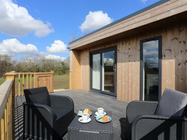 An outdoor wooden deck with black wicker chairs and a table with coffee cups and cakes at The Swift in Wem