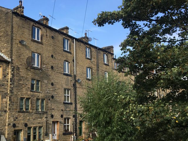 A stone apartment building with multiple windows and antennae next to tall trees at Up-Top Cottage in Peak District
