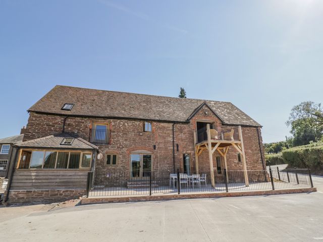 A stone building with a patio table and chairs and a small wooden balcony at Munderfield Mill in Munderfield near Bishops Frome