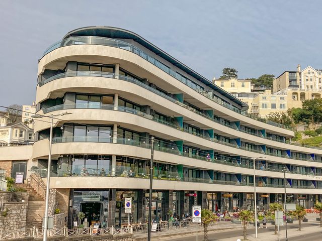 A modern multi-story building with curved balconies and shops on the ground floor at 18 Abbey Sands in Torquay