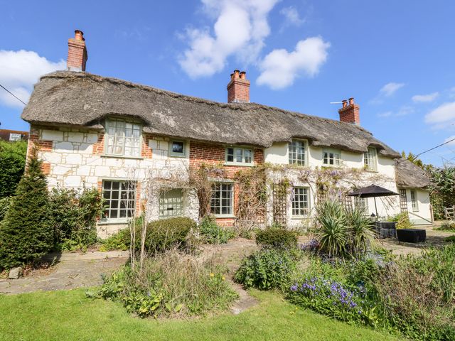 A thatched cottage with brick chimneys windows and garden plants at 19 Clatterford Shute in Carisbrooke