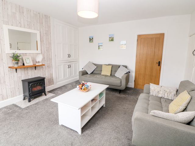 A living room with two grey sofas a white coffee table and a small electric stove at Harpur Cottage in Buxton
