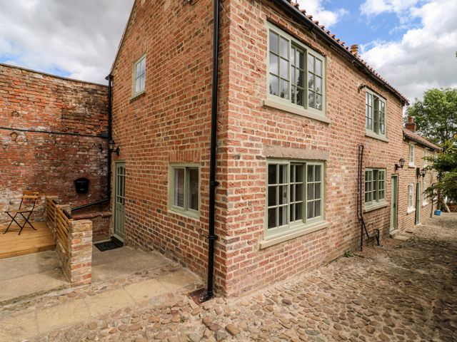 A brick house with green window frames and doors on a cobblestone street at Kemps Yard Retreat in Thirsk