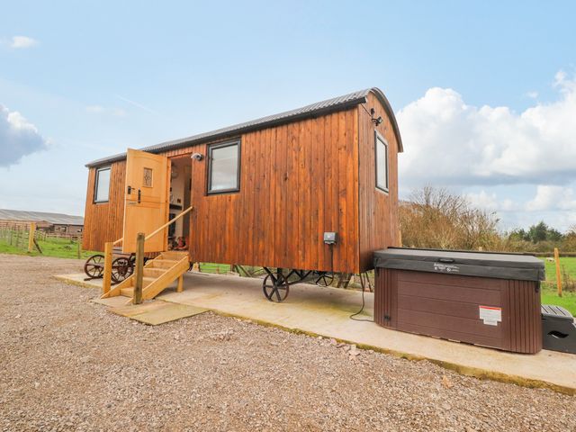A wooden shepherds hut with stairs and an open door next to a hot tub on a concrete pad at Hillcrest Shepherds Hut in Chipping