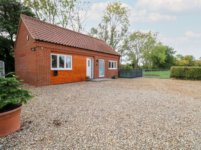 A brick house with a tiled roof and a gravel driveway with trees and a metal gate at Robins Nest in Brisley near North Elmham