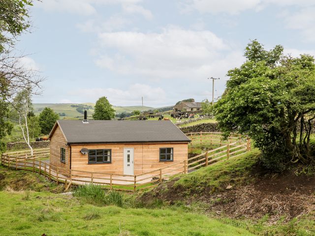 A wooden house with a fenced yard in a rural area with hills and trees at Brookside in Hayfield