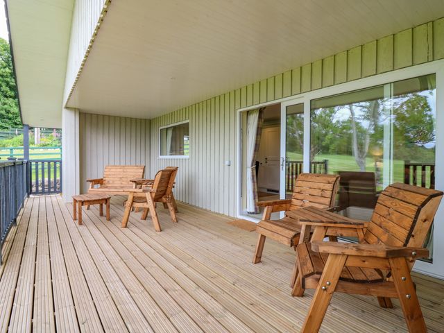 A covered patio with wooden chairs and tables overlooking a grassy area at The Lodge in Blairgowrie
