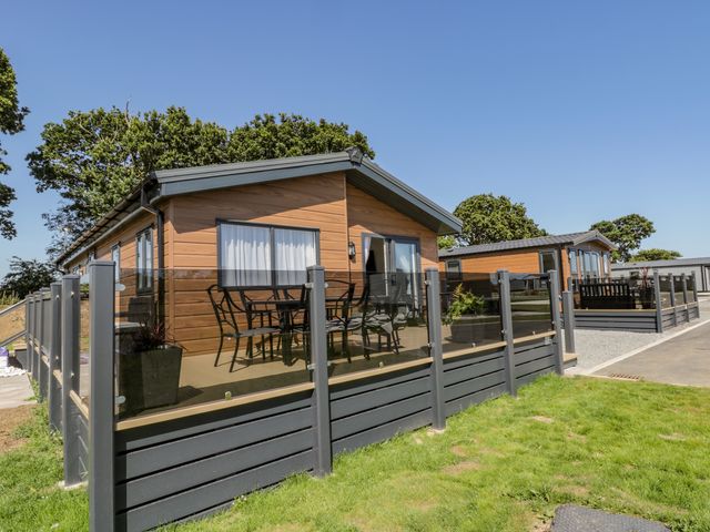 Two wooden lodges with glass fenced patios and outdoor furniture on a grassy area at Brighter Daze in Carnaby near Bridlington