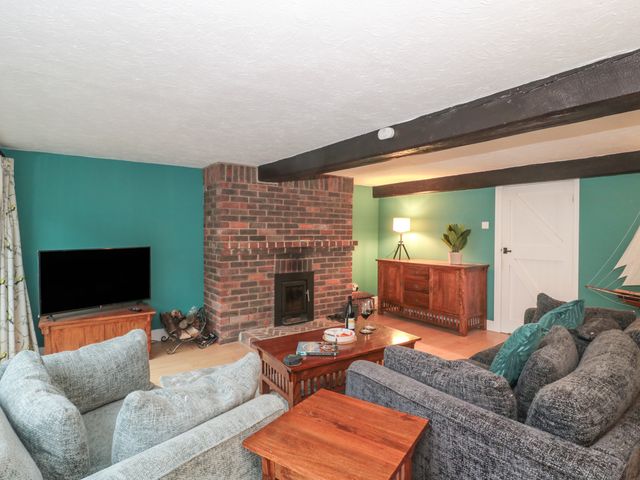 A living room with sofas facing a brick fireplace and a TV on a wooden cabinet at The Grain Store in Weymouth