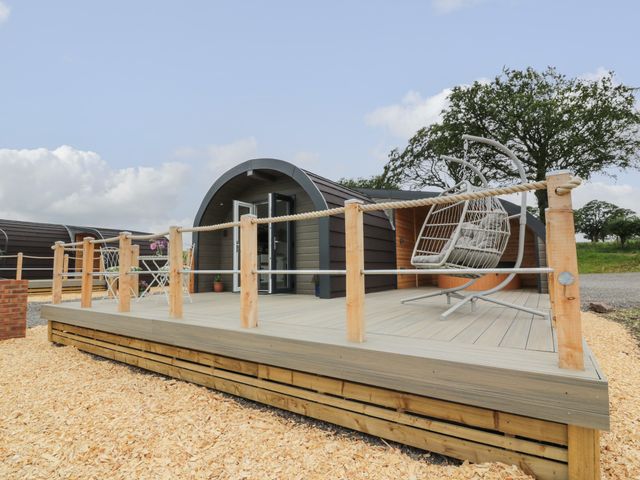 An outdoor deck area with a hanging chair and a small table with chairs in front of a pod-style building at Laird Lodge 1 in Lochmaben