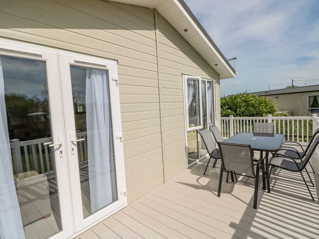 An outdoor deck with a glass table and six chairs next to a beige building at The Last Resort in Pendine