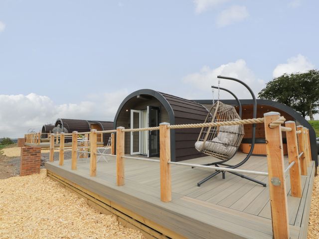 A wooden deck with hanging chair and seating area outside curved small cabins at Laird Lodge 3 in Lochmaben