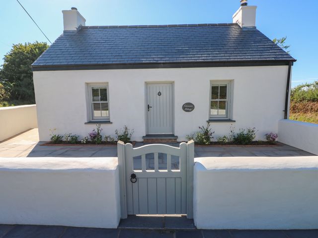 A white cottage with a grey roof and gate with flowers along the front at Catamouse in Milford Haven