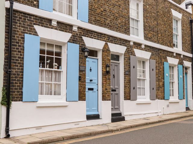 A row of brick townhouses with blue and gray doors and shutters on a street at Kentish Knock in Deal