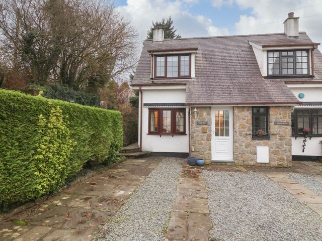 A stone and white exterior semi detached house with gravel driveway and trimmed hedge at Craig Mawr in Benllech