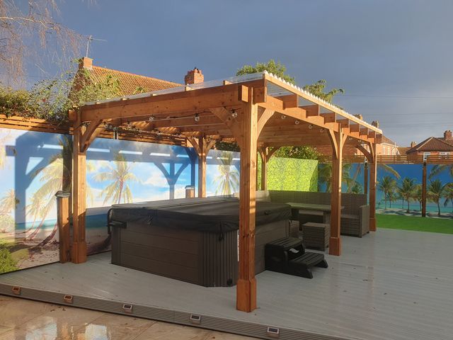 An outdoor patio with a covered hot tub and wicker seating under a wooden pergola at Seabar in Burnham-On-Sea