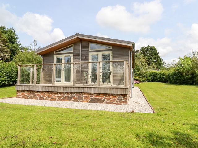 A wooden cabin with glass doors and a small deck with two chairs and a table in a grassy yard at 6 Southern Place in Dobwalls