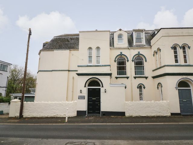 The exterior view of a cream colored house with arched windows and black doors at Beaufort House in Ilfracombe