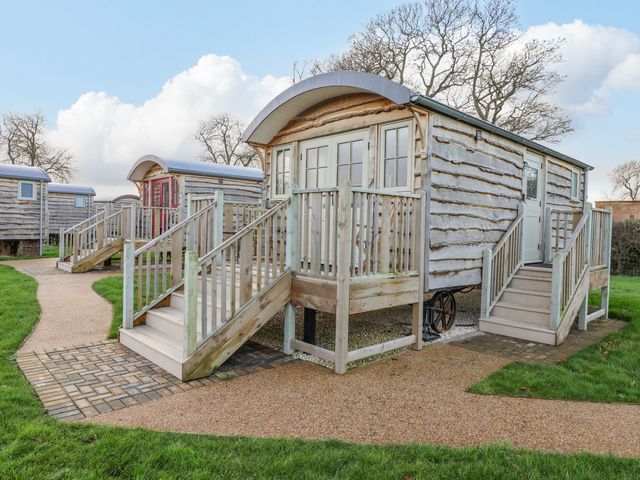 A group of wooden shepherd huts with stairs and railings on a grassy area at Folklore in Bolton Percy near Tadcaster