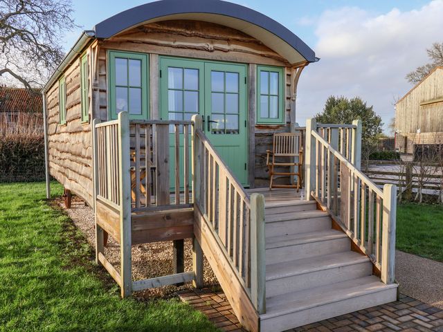 A wooden cabin with green doors and windows a porch with stairs and wooden chairs at The Studio in Bolton Percy near Tadcaster