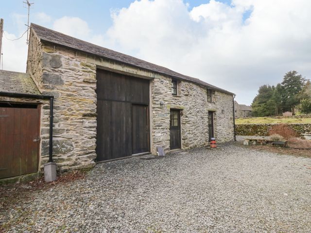 A stone building with wooden doors and windows on a gravel area with trees in the background at Myras View in Newby Bridge