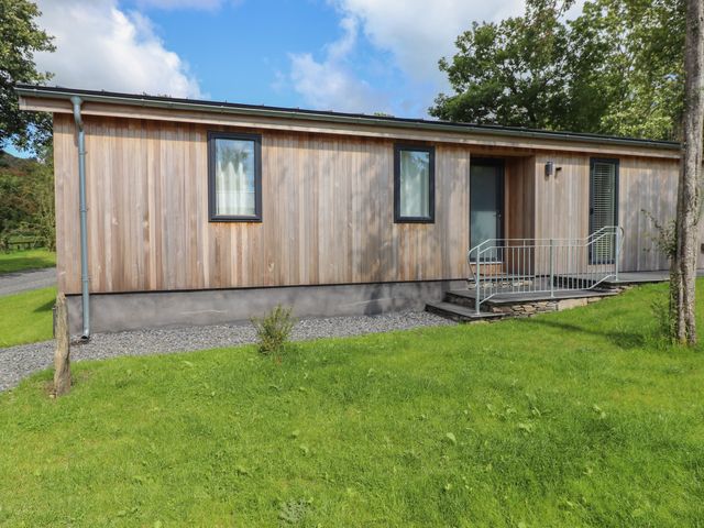 A small wooden house with two windows a door and a metal railing ramp in a grassy area at The Beeches in Haverthwaite