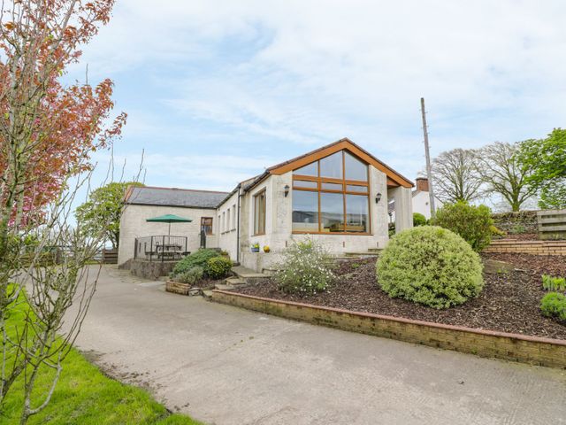 An exterior view of a single-story house with large windows a concrete driveway and landscaped garden at Laird House in Lochmaben
