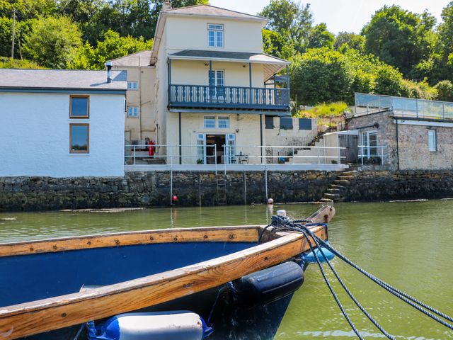 A boat tied to a dock in front of a multi-story house by the water at Shipwrights in Galmpton Torbay