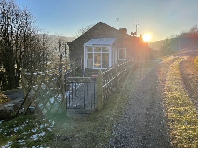 A stone house with a metal gate and wooden fence along a dirt road at Joyces Cottage 2 Brown Hill in Low Row near Reeth