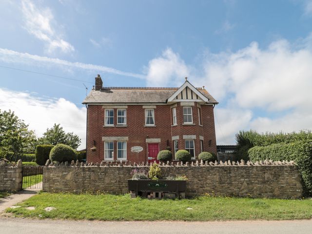 A two story brick house with white framed windows red door front garden and stone wall at The Farmhouse in Swanage