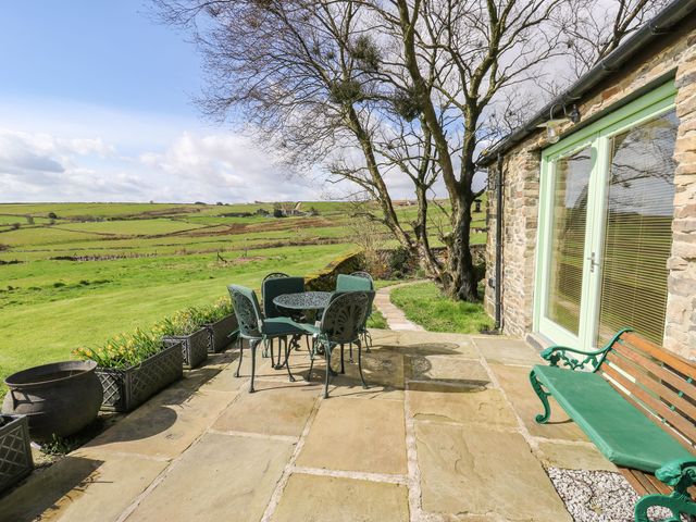 A stone patio with a metal table and chairs a bench and large windows overlooking green fields at The Barn at Crow Hill Shaw Farm in Sowerby Bridge