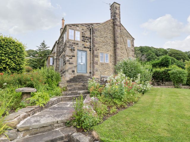 A stone house with a blue door surrounded by a garden and stone steps at Fern Cottage in Baslow